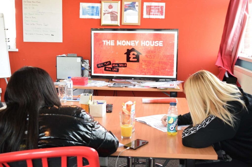 Participants sat at a desk writing on worksheets at MyBnk's fuel poverty programme, The Money House