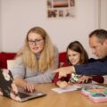 Two adults and a child sat around a dining table looking at a laptop together