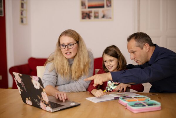 Two adults and a child sat around a dining table looking at a laptop together