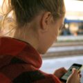 young person standing on a train platform looking at mobile phone