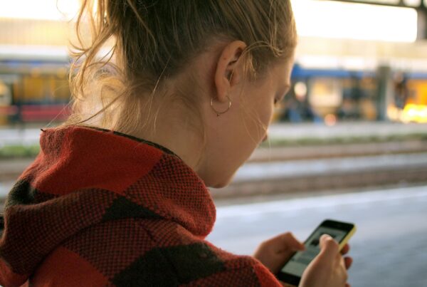 young person standing on a train platform looking at mobile phone