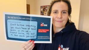 Selfie of a woman holding a sheet of paper with a top tip for online safety written on it, for Global Money Week